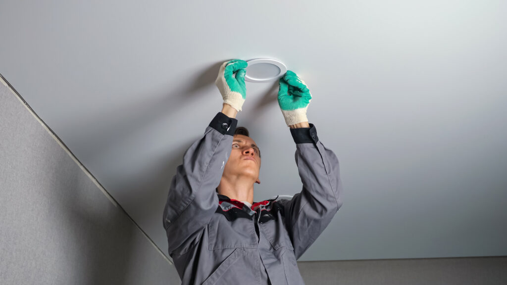 Electrician installing canned recessed lighting in a white living room ceiling.