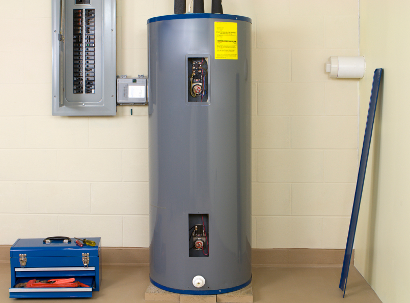 A gray tank water heater in a home's basement, with blue toolbox on the ground to the left.